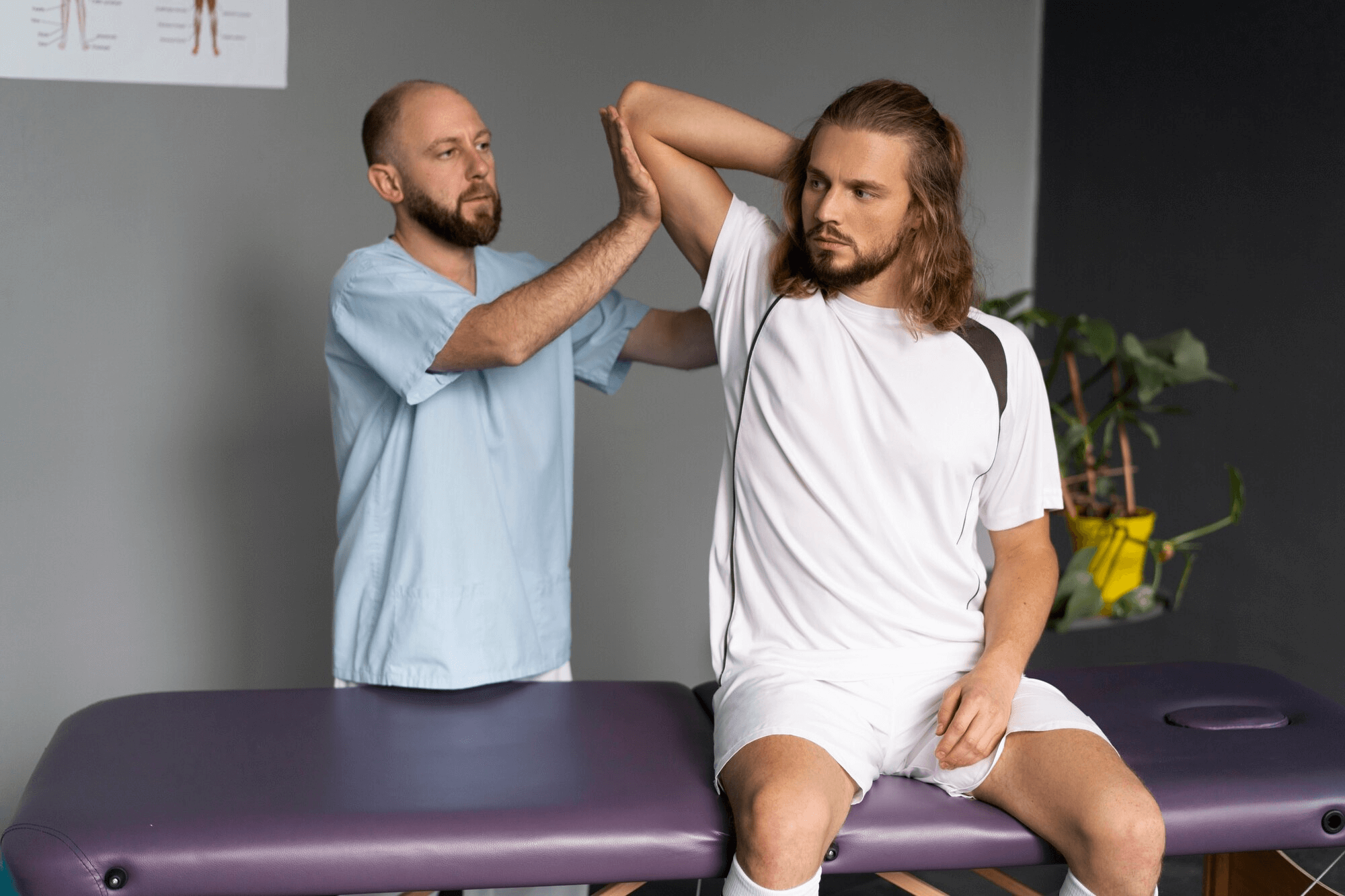 A physical therapist assists a man with an arm stretch exercise on an examination table in a clinical setting, addressing back pain resulting from a recent car accident.