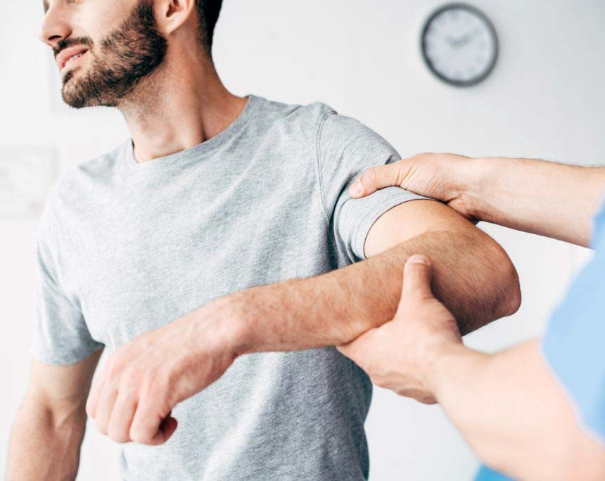 A person in a gray shirt receives a physical therapy session, with a chiropractor skillfully manipulating their arm. The individual, likely recovering from back pain caused by a car accident, appears focused as the clock ticks quietly on the wall in the background.