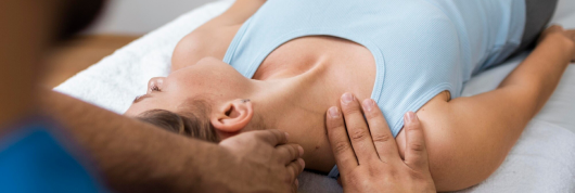A person, recovering from a car accident, receives a neck and shoulder massage to alleviate back pain while lying on a table, wearing a sleeveless top.